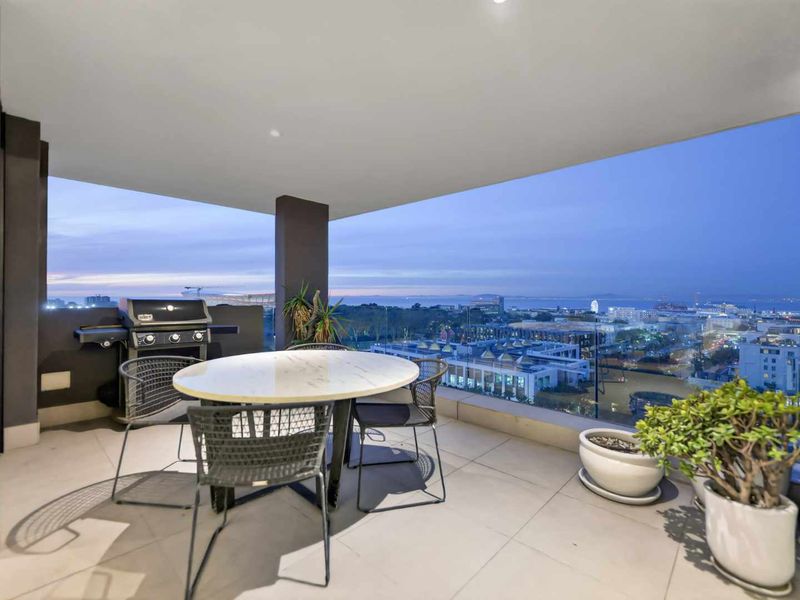 Spacious covered balcony featuring modern tiled flooring, a glass balustrade, and expansive panoramic city and coastal views.