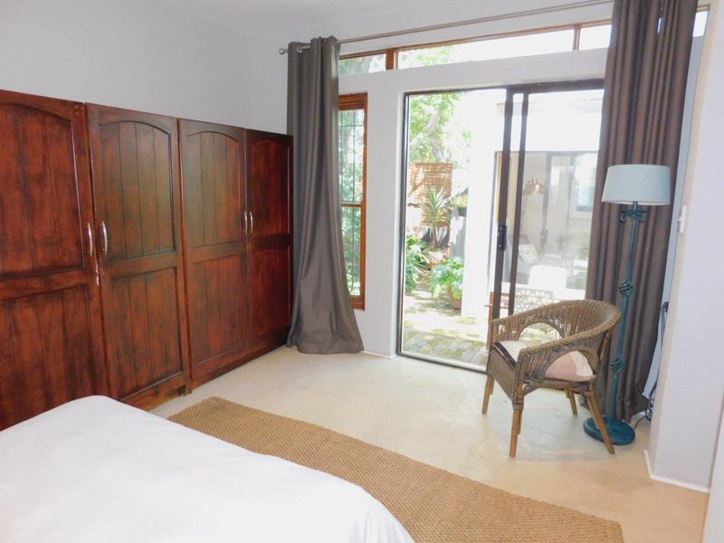 Bedroom featuring built-in wooden cupboards, neutral flooring, and a sliding glass door providing direct access to the garden area.