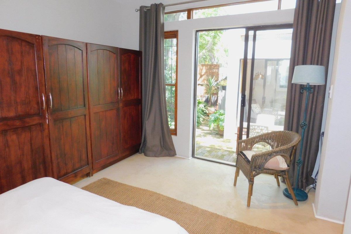 Bedroom featuring built-in wooden cupboards, neutral flooring, and a sliding glass door providing direct access to the garden area.