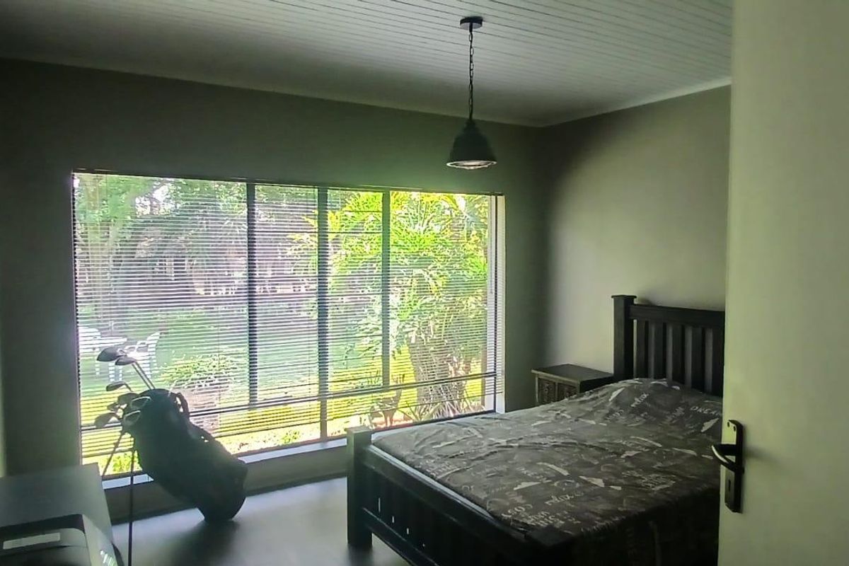 A bedroom featuring large windows with horizontal blinds, a tongue-and-groove ceiling, and a pendant light fixture.