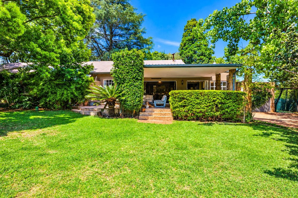 A view of the rear exterior featuring a well-maintained lawn, mature garden landscaping, and a covered patio area with tiled steps.