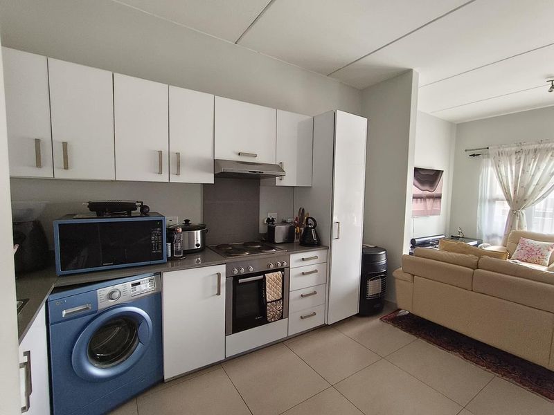 Open-plan kitchen and living area featuring white cabinetry, built-in oven, electric hob, and tiled flooring, seamlessly connecting to the adjacent lounge space.
