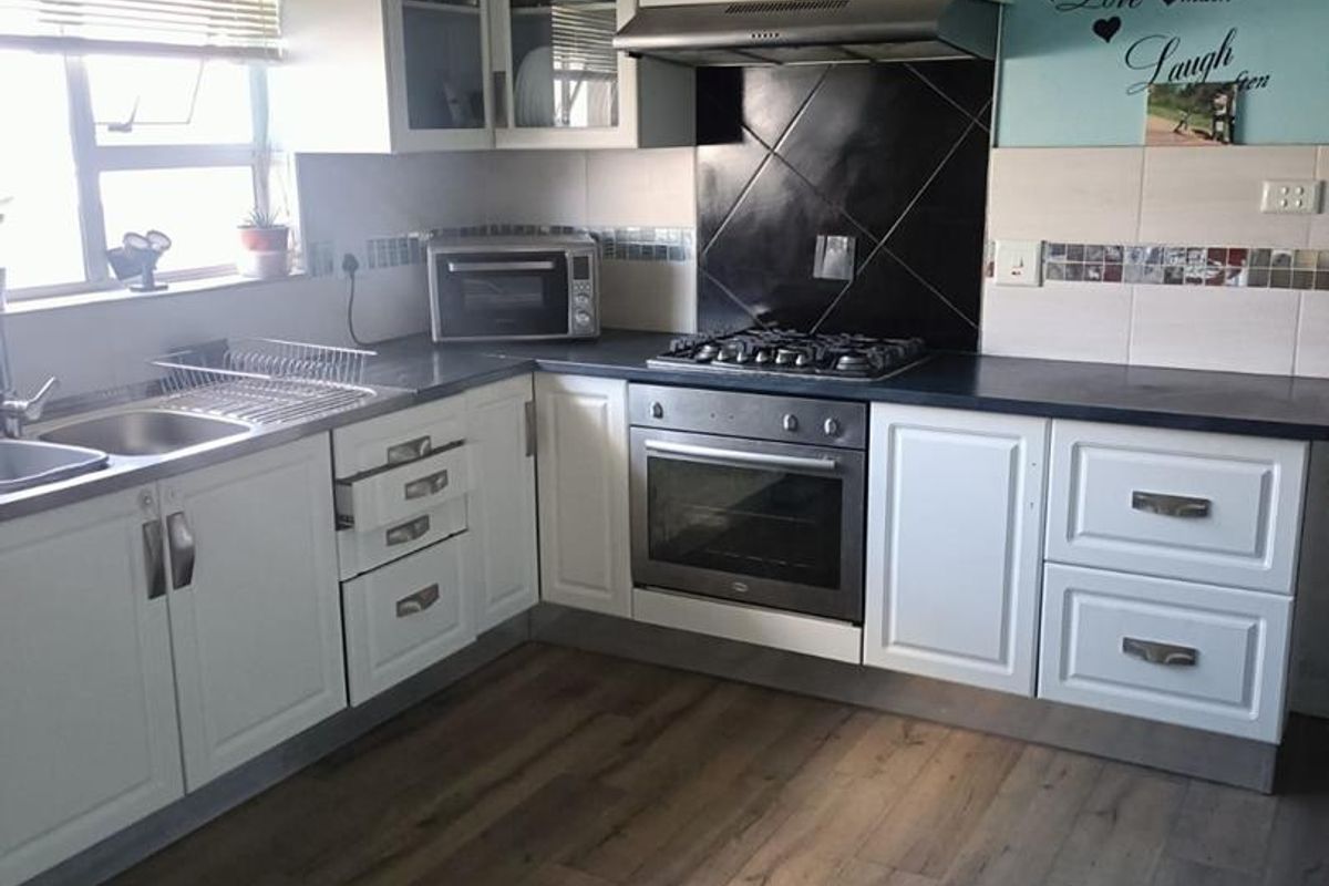 A functional kitchen featuring white cabinetry, dark countertops, a built-in oven, gas hob, extractor fan, and wood-look laminate flooring.