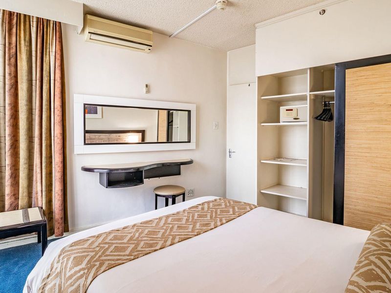 A functional bedroom featuring a built-in wardrobe with shelving, a wall-mounted vanity, and an integrated air conditioning unit.