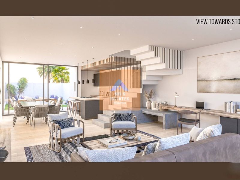Modern open-plan living area featuring a sleek kitchen, integrated staircase, and seamless flow to the outdoor patio and garden through large sliding doors.