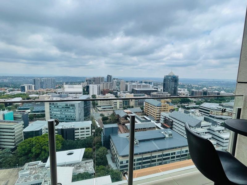 Elevated city skyline view captured from a modern apartment balcony featuring a sleek glass and stainless steel balustrade.