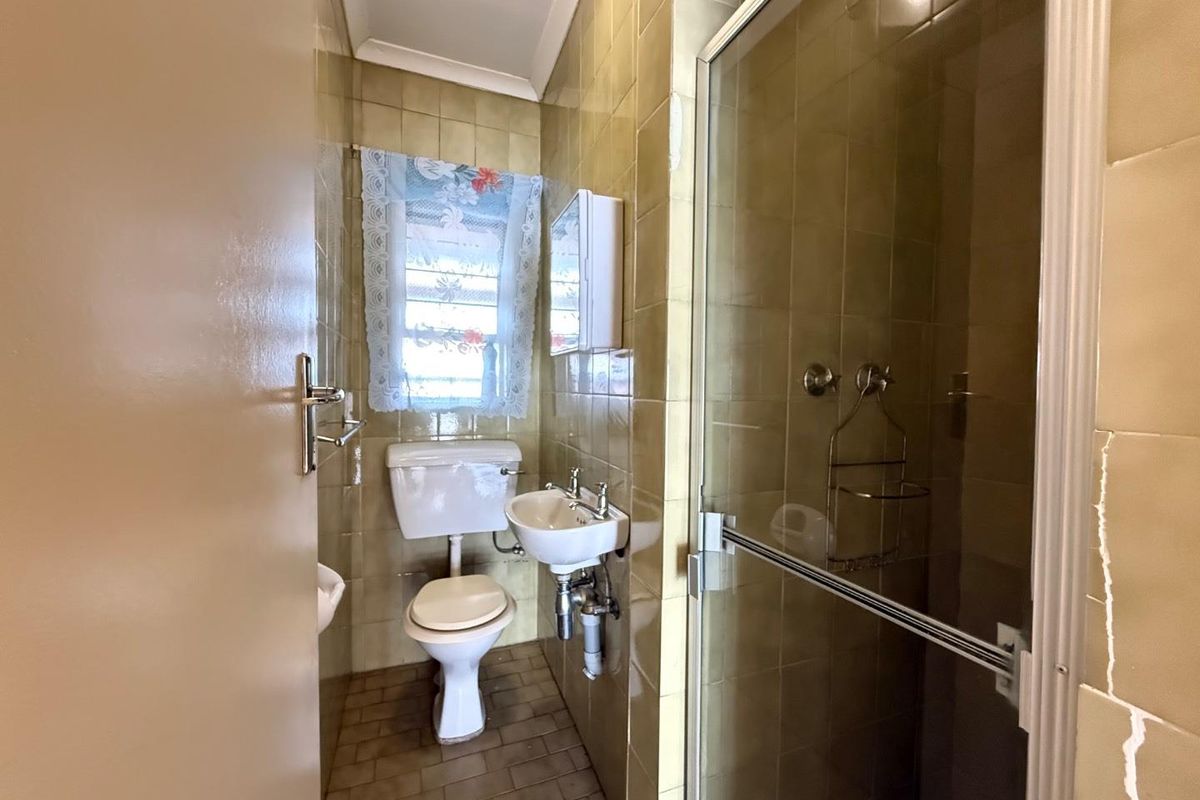 A compact bathroom featuring a shower enclosure, wall-mounted basin, and toilet, finished with dated ceramic wall tiles.