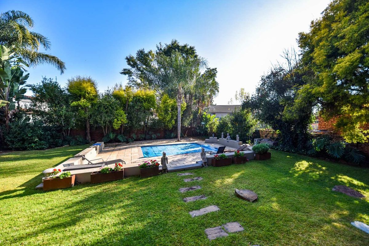 A well-maintained backyard featuring a swimming pool with a paved deck, surrounded by a lush landscaped garden and mature trees.
