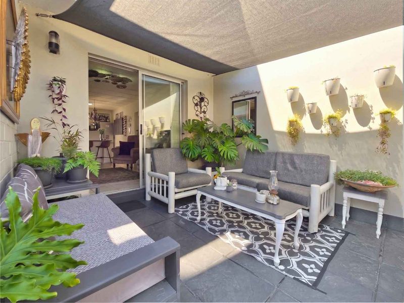 A well-maintained covered patio featuring stone tile flooring, a shade sail, and direct access to the interior living space via a sliding glass door.
