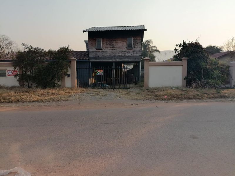 Front view of a property featuring a metal gate, perimeter wall, and a two-story structure with weathered timber cladding and a corrugated metal roof.