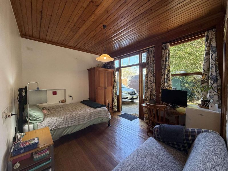 A bedroom featuring timber flooring and a timber-paneled ceiling, with direct access to an outdoor area through a glass-paneled door.