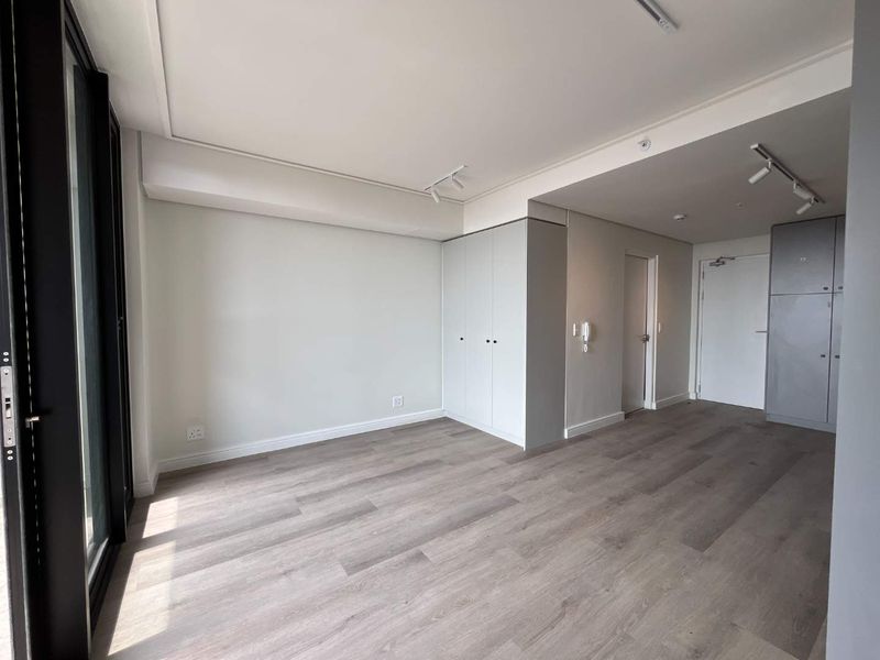 A bright, modern, and empty living area featuring light wood-look laminate flooring, built-in storage cupboards, and access to an outdoor space via sliding doors.