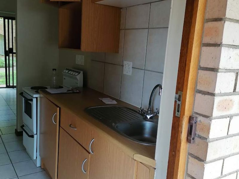Compact kitchen featuring laminate cabinetry, stainless steel sink, tiled splashback, and a freestanding stove with ceramic floor tiles.