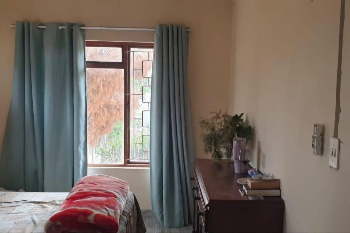 A standard bedroom featuring a window with curtains and visible wall surface finishes.