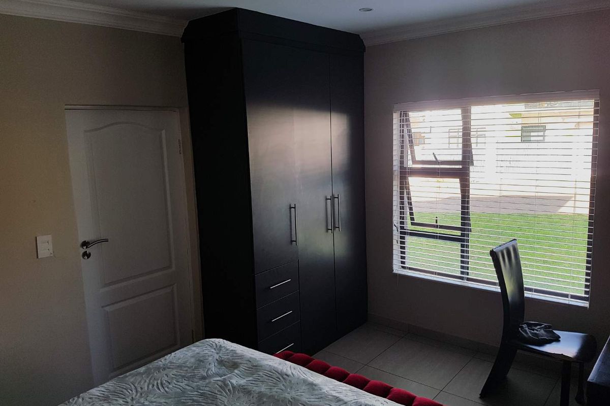 A bedroom featuring built-in dark cabinetry, tiled flooring, and a window with fitted blinds, offering a functional and well-maintained living space.