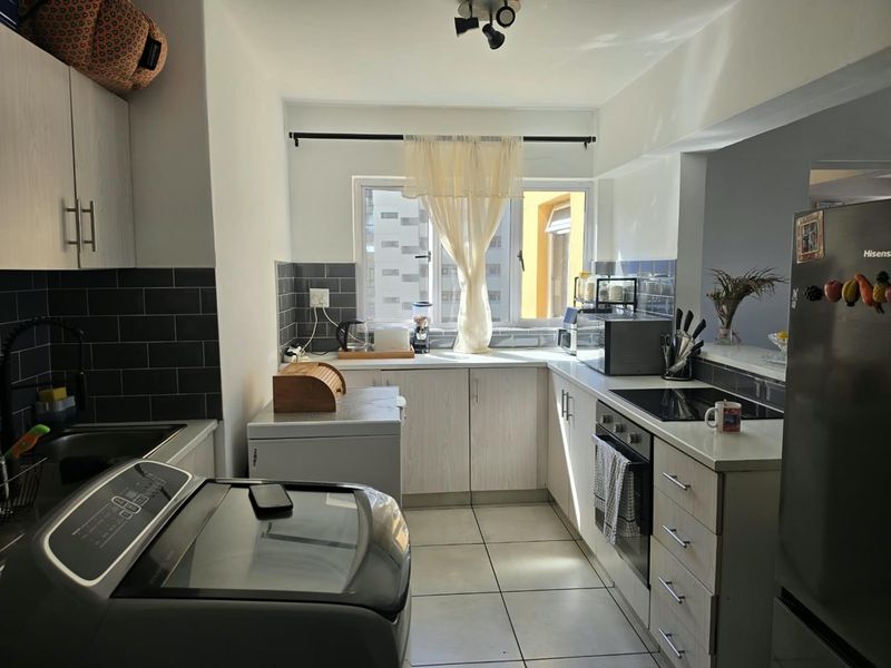 A functional kitchen featuring light-toned cabinetry, dark tiled backsplash, ceramic floor tiles, and integrated cooking appliances including an oven and hob.