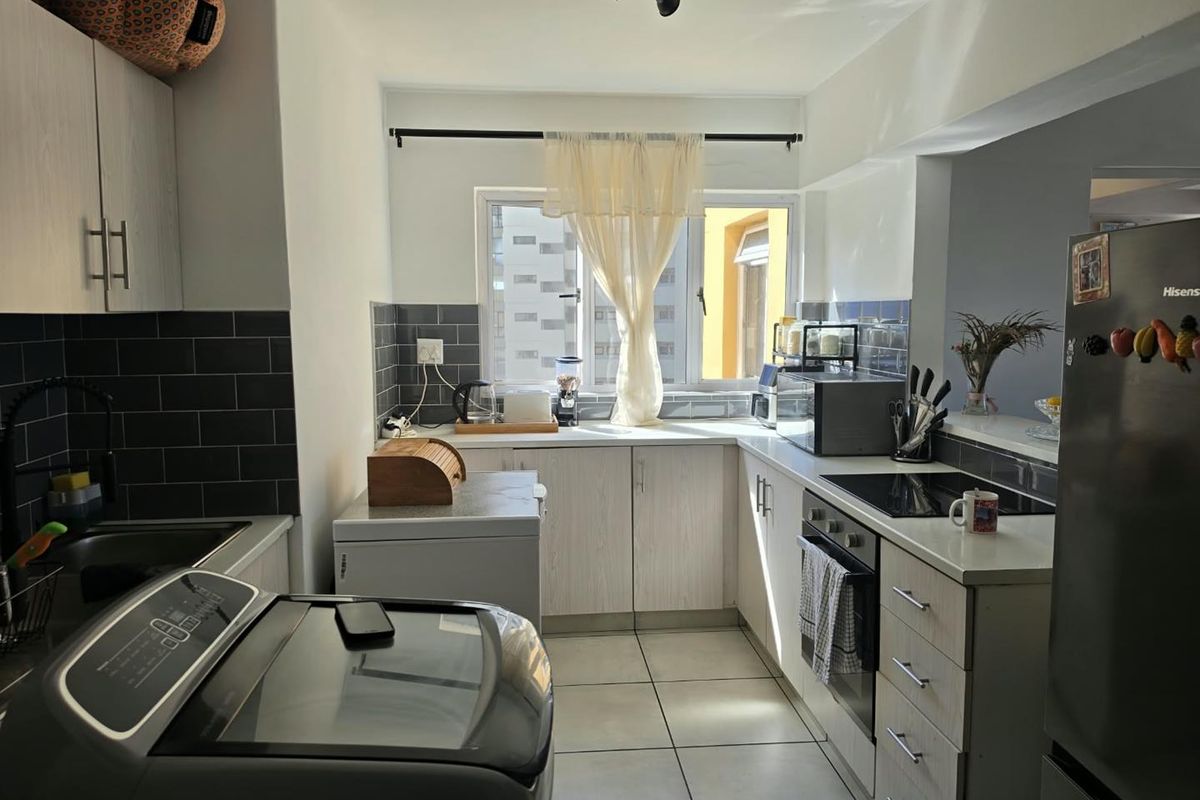 A functional kitchen featuring light-toned cabinetry, dark tiled backsplash, ceramic floor tiles, and integrated cooking appliances including an oven and hob.