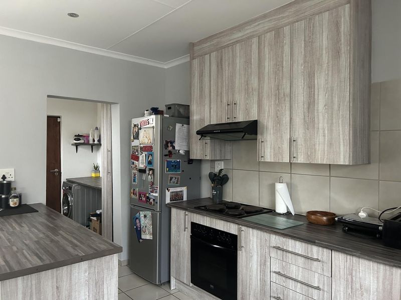 Modern kitchen featuring wood-look laminate cabinetry, dark countertops, built-in oven, and hob, with an adjacent scullery area visible through the doorway.