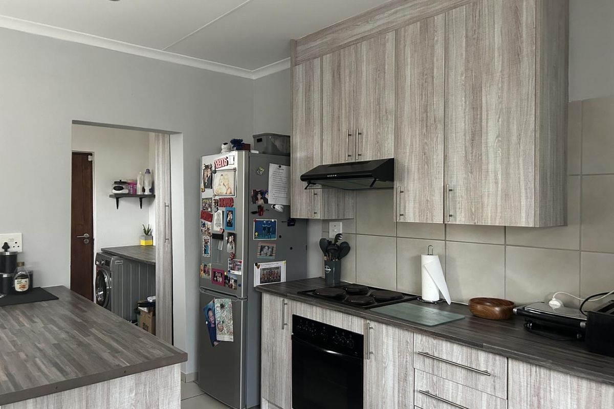 Modern kitchen featuring wood-look laminate cabinetry, dark countertops, built-in oven, and hob, with an adjacent scullery area visible through the doorway.