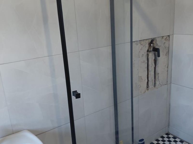 Bathroom featuring a glass shower enclosure with black framing, pedestal basin, and tiled finishes, currently requiring repair to the shower wall area.
