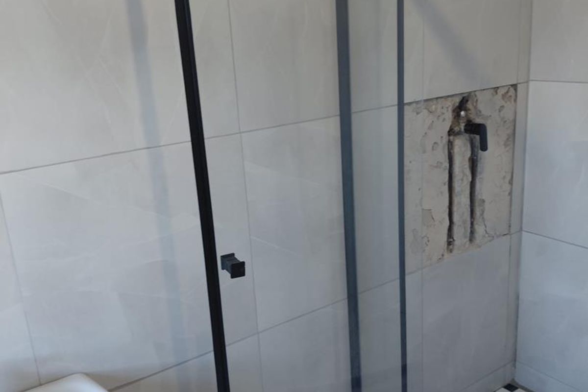 Bathroom featuring a glass shower enclosure with black framing, pedestal basin, and tiled finishes, currently requiring repair to the shower wall area.