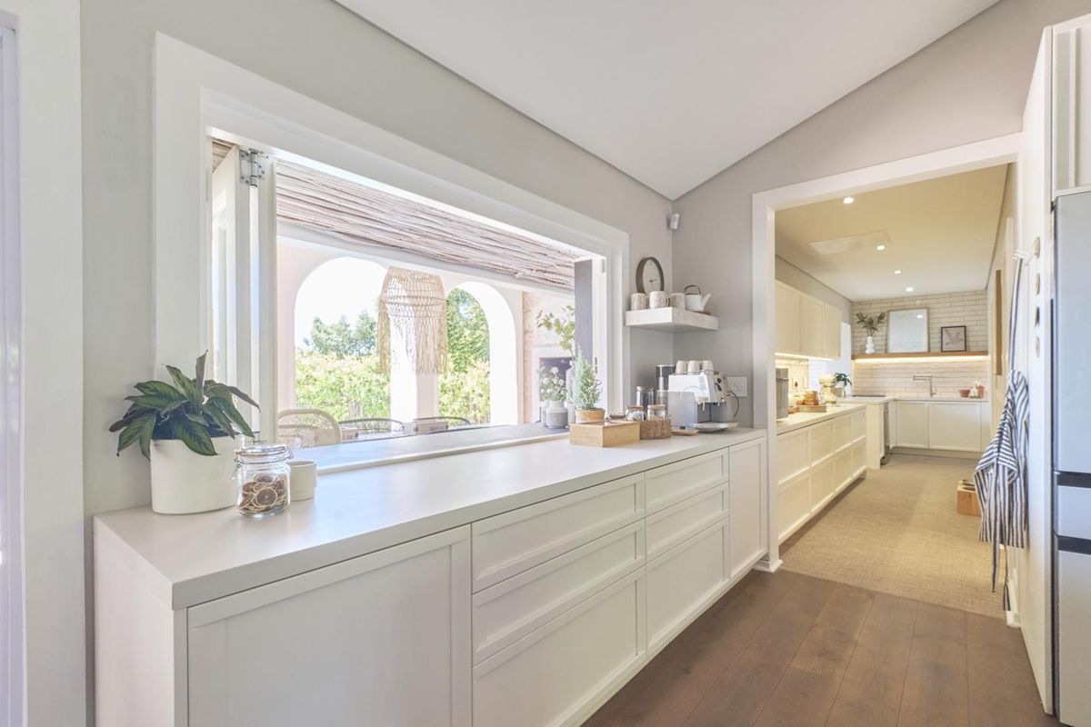 Modern kitchen featuring sleek built-in cabinetry, stone countertops, and a large bi-fold window opening to an outdoor patio area.