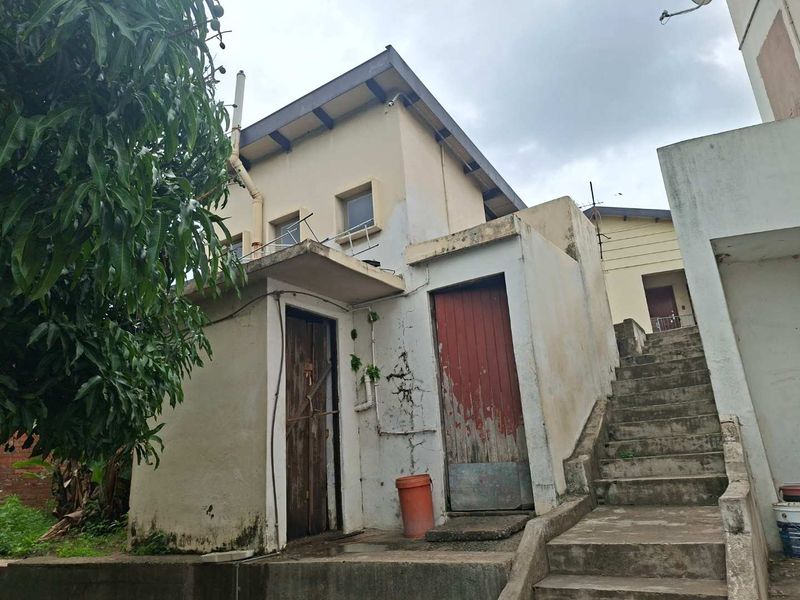 Rear exterior view of the property showing concrete stairs, weathered exterior walls, and multiple access doors requiring maintenance.