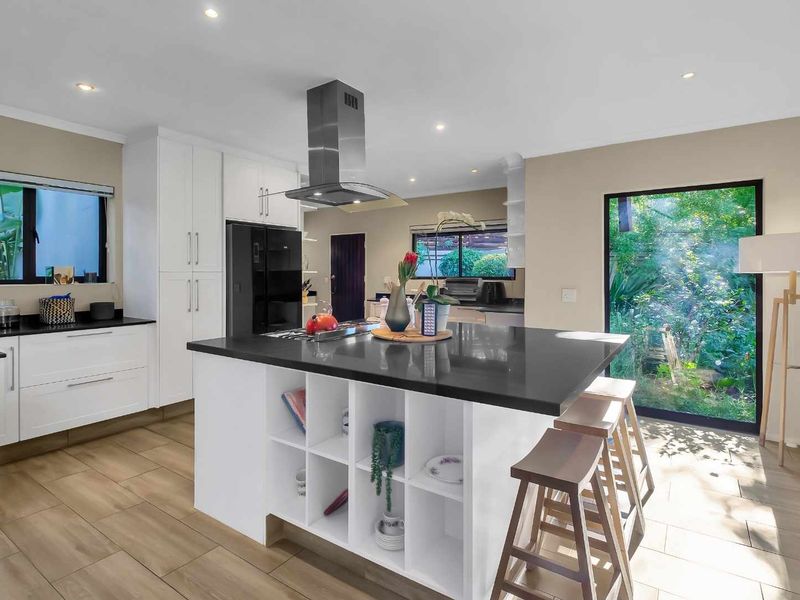 Modern kitchen featuring a central island with stone countertops, white cabinetry, stainless steel extractor fan, and large windows overlooking the garden.