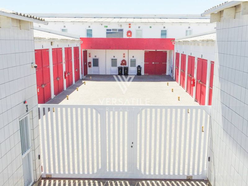 A secure industrial courtyard featuring multiple storage or workshop units with red roller shutter doors and paved access.