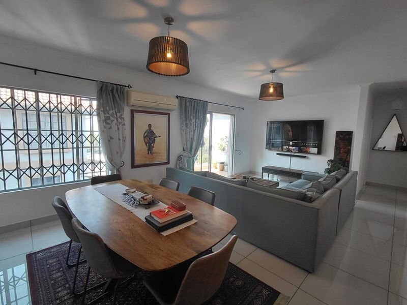 Spacious open-plan living and dining area featuring tiled flooring, split-system air conditioning, and direct access to an outdoor balcony through sliding glass doors.