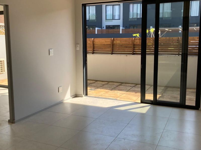 An empty, modern living area featuring neutral tiled flooring and large sliding glass doors that open onto a private patio.