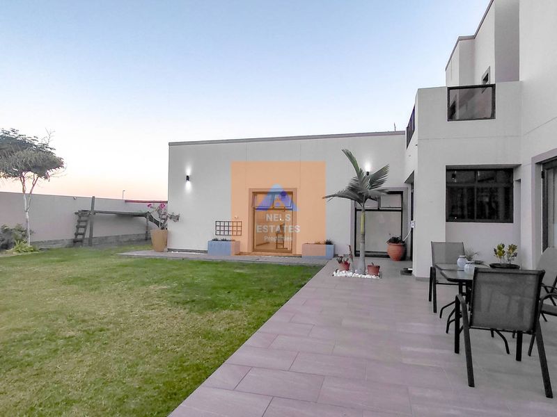 A well-maintained rear exterior featuring a paved patio area, lawn, and modern building facade with sliding glass doors.