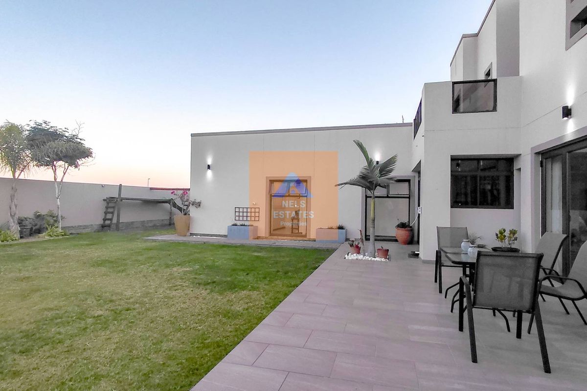 A well-maintained rear exterior featuring a paved patio area, lawn, and modern building facade with sliding glass doors.