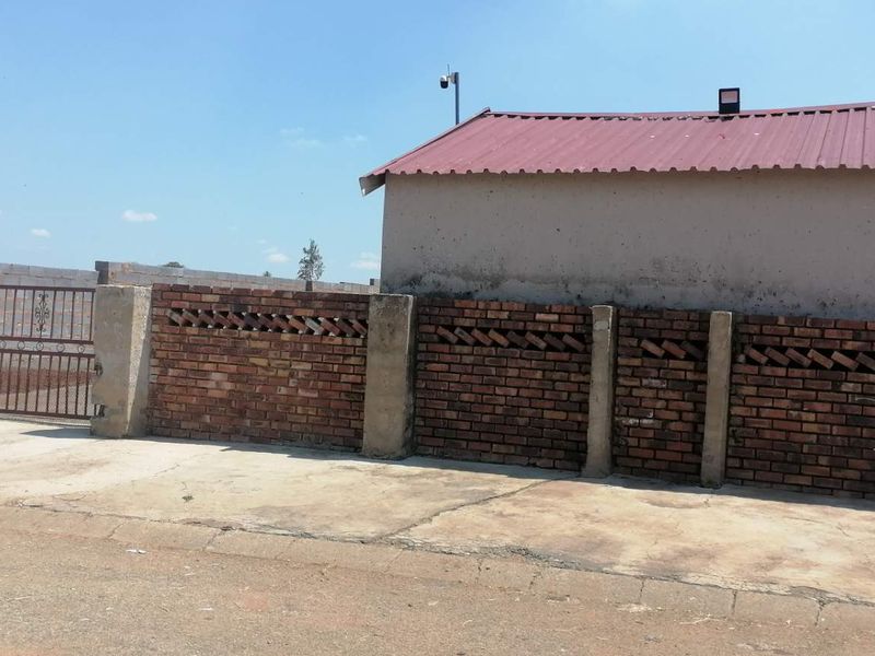 Front exterior view showing a concrete driveway, brick boundary wall with decorative detailing, and a metal gate leading to the property.