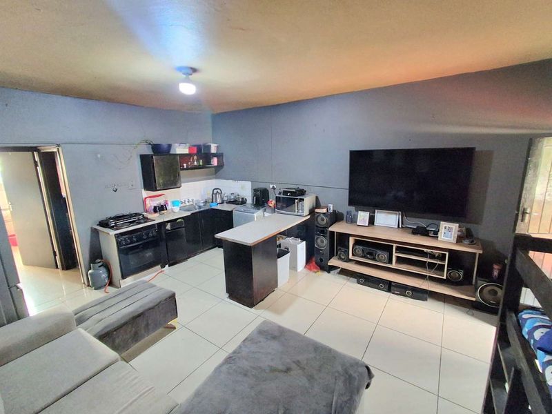 Open-plan living area featuring a compact kitchen with built-in cabinetry, gas hob, oven, and tiled flooring throughout the combined space.
