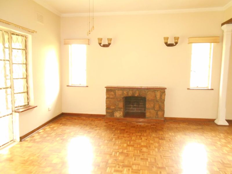 Spacious living room featuring classic parquet flooring, a stone fireplace, and wall sconces, offering a bright and open area ready for personalization.