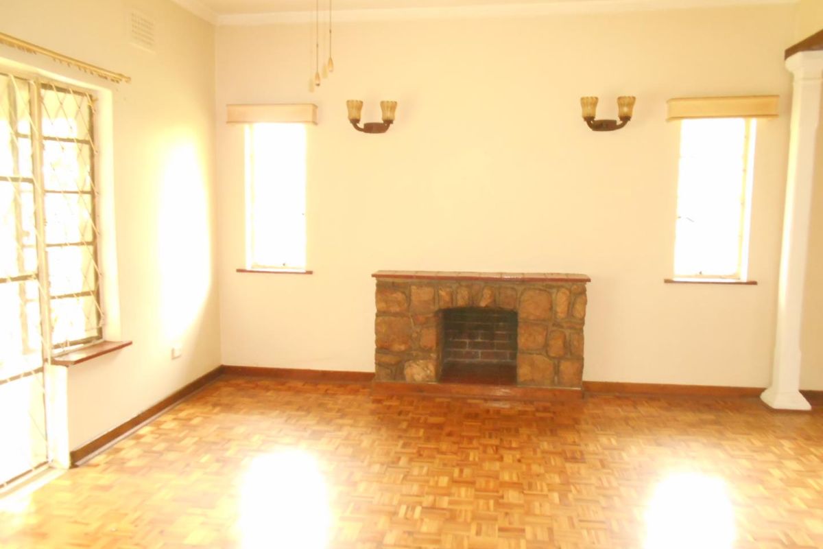 Spacious living room featuring classic parquet flooring, a stone fireplace, and wall sconces, offering a bright and open area ready for personalization.