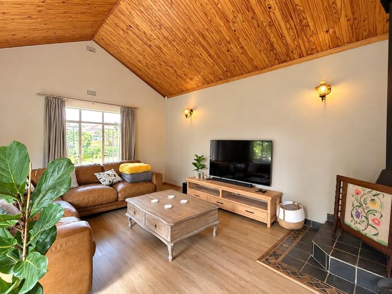 Spacious living room featuring a high vaulted timber ceiling, laminate flooring, and a cozy wood-burning fireplace with a tiled hearth.
