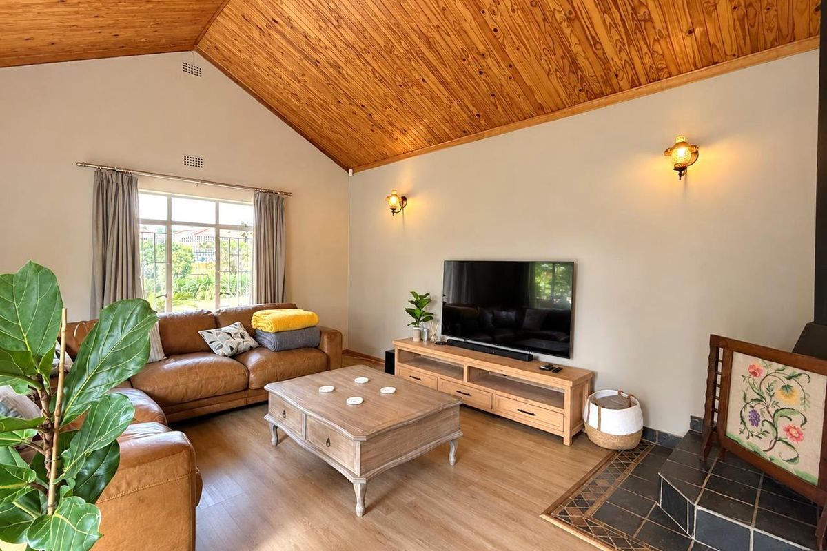 Spacious living room featuring a high vaulted timber ceiling, laminate flooring, and a cozy wood-burning fireplace with a tiled hearth.