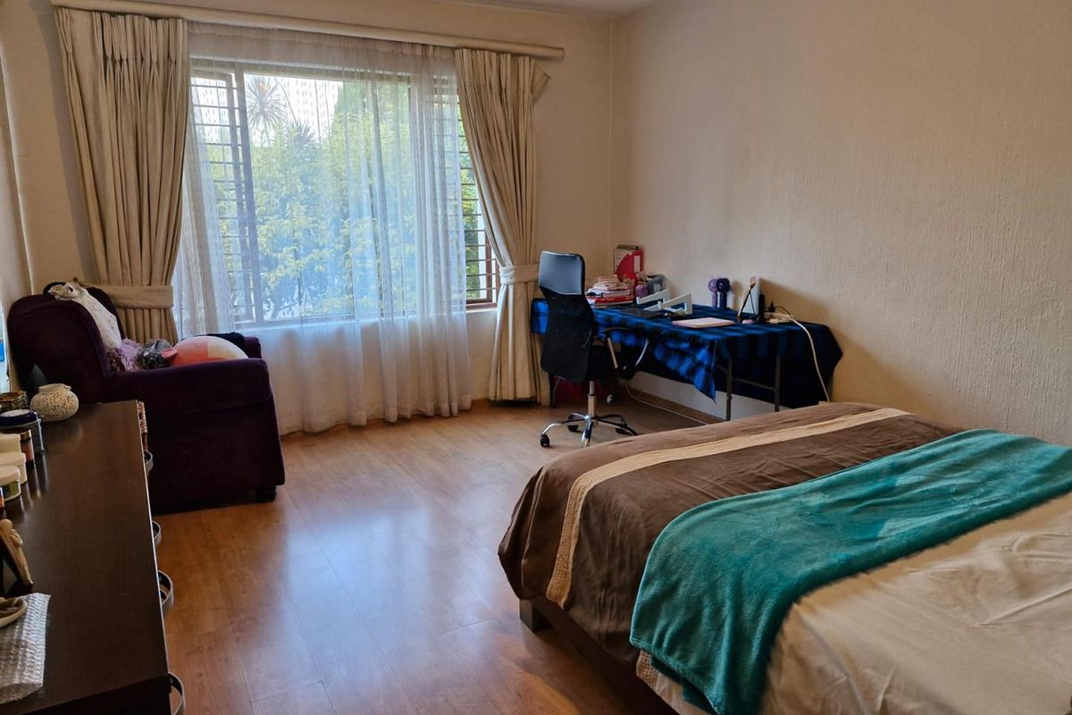 A spacious bedroom featuring laminate flooring, large windows with curtains, and security bars, offering a comfortable and functional living space.