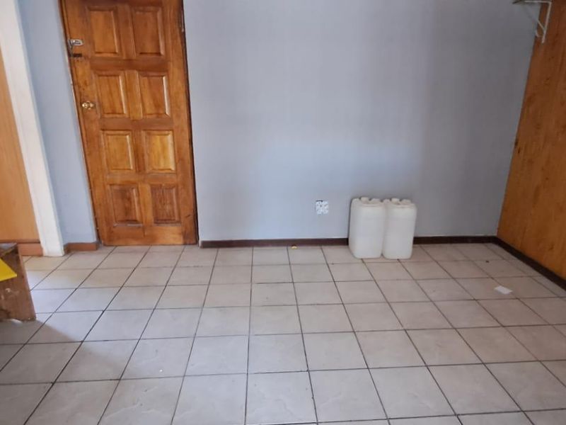 An empty bedroom featuring tiled flooring, a wooden door, and timber wall paneling, offering a blank canvas for potential renovation or restyling.