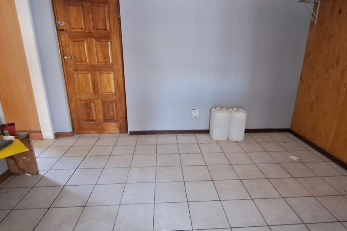 An empty bedroom featuring tiled flooring, a wooden door, and timber wall paneling, offering a blank canvas for potential renovation or restyling.