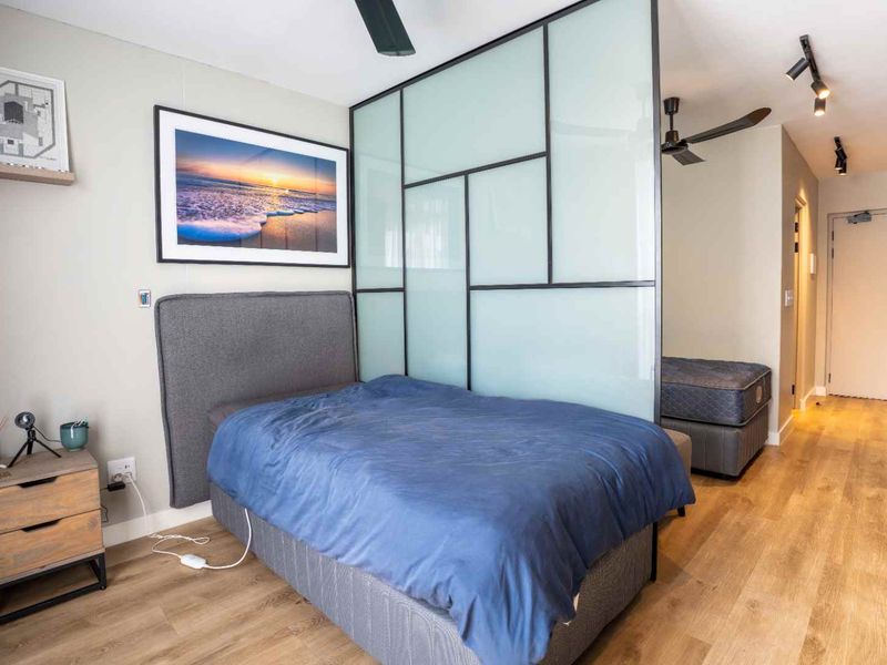 A modern bedroom featuring a stylish frosted glass partition, laminate flooring, and integrated ceiling fan, creating a contemporary and functional living space.