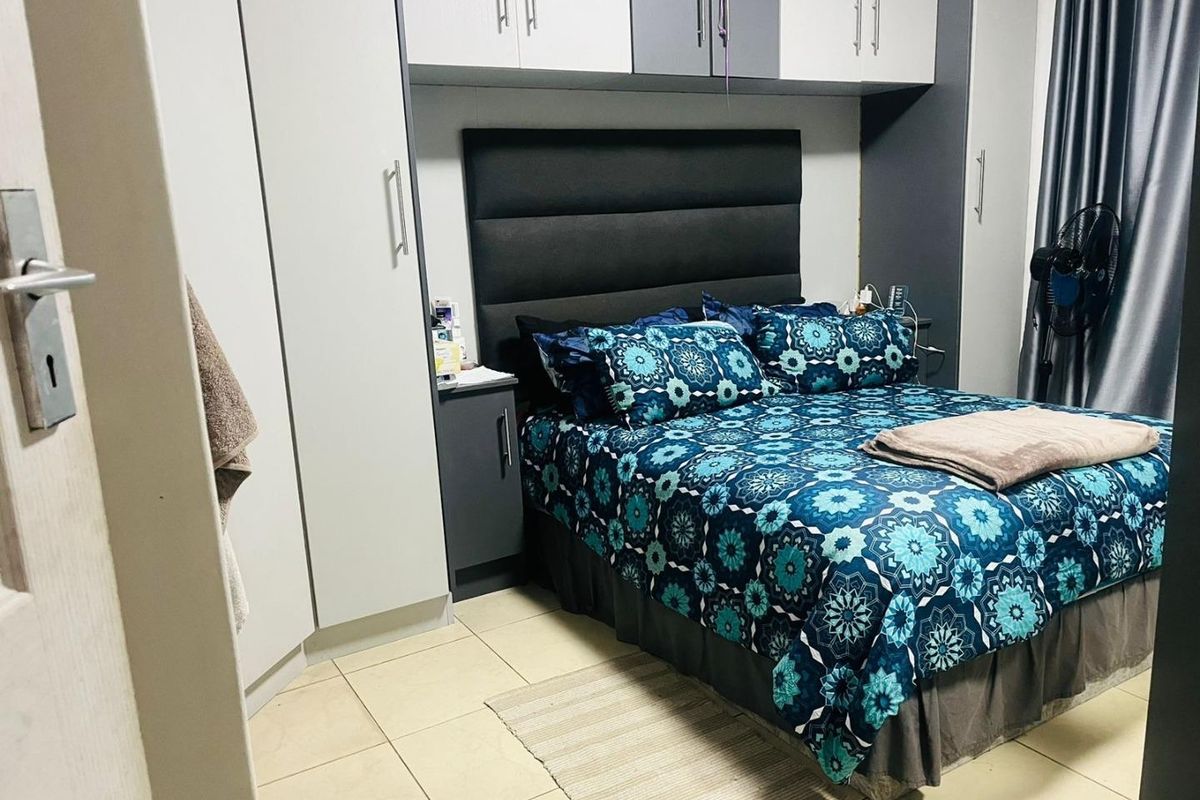 A well-maintained bedroom featuring built-in cupboards with overhead storage cabinetry and neutral tiled flooring.