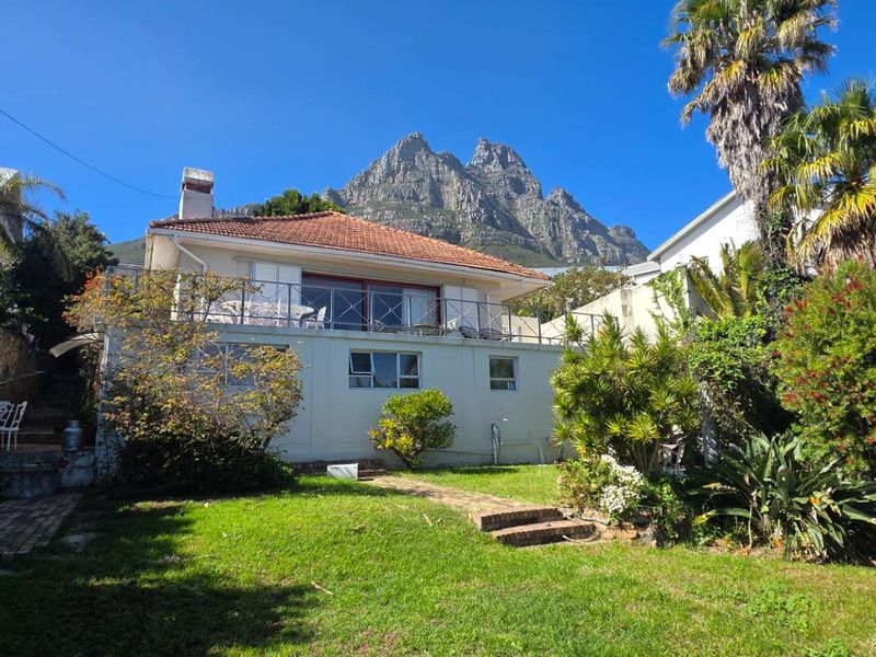 Rear view of the house featuring a raised balcony, terracotta roof, and established garden with mountain views.