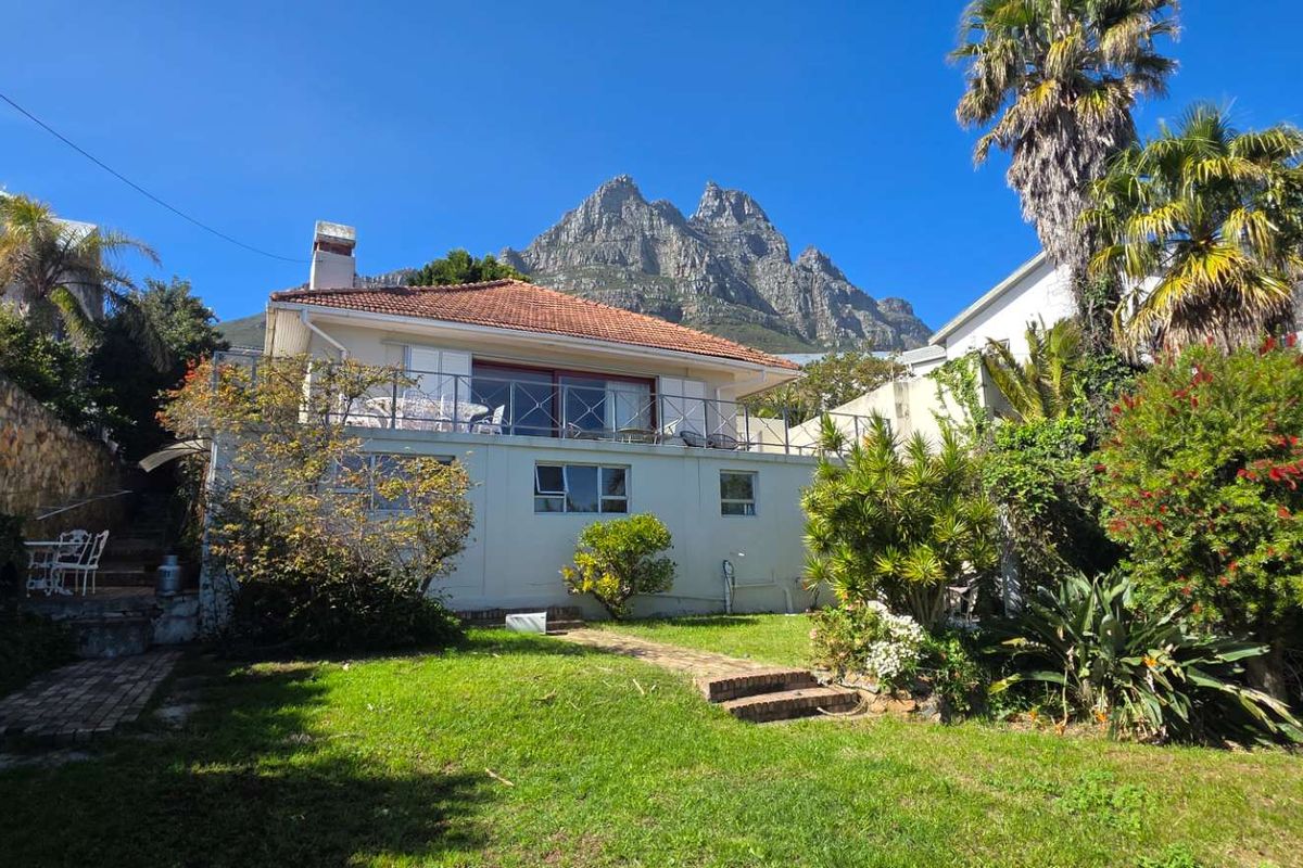 Rear view of the house featuring a raised balcony, terracotta roof, and established garden with mountain views.