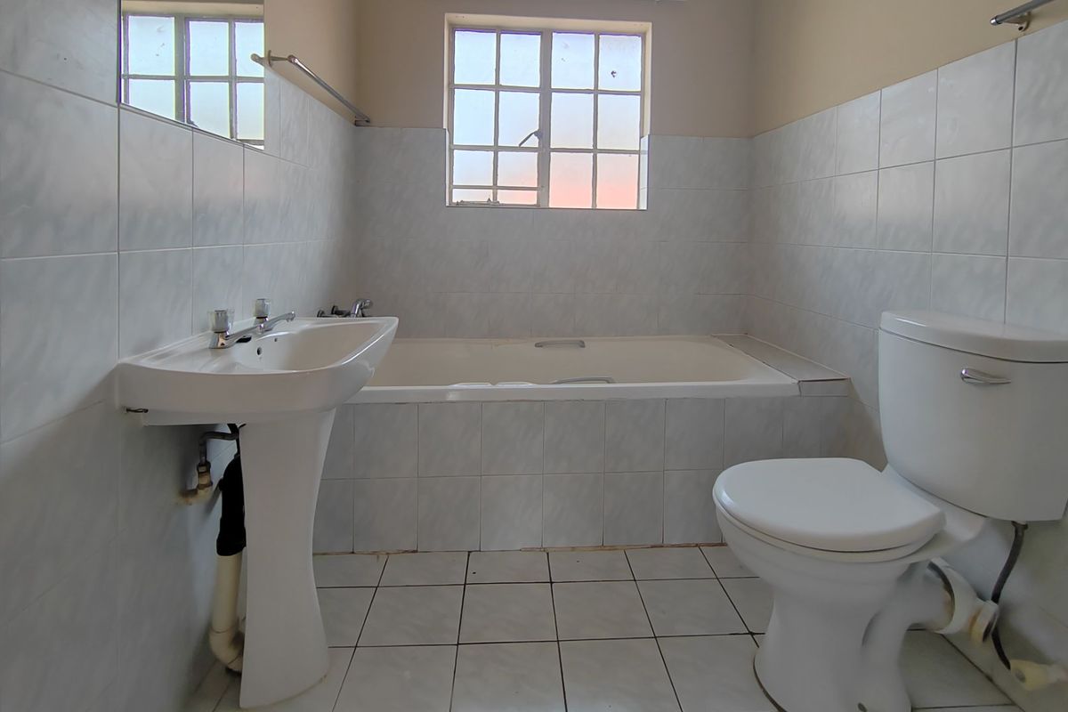A functional bathroom featuring a pedestal basin, built-in bathtub, and toilet with neutral wall and floor tiling.