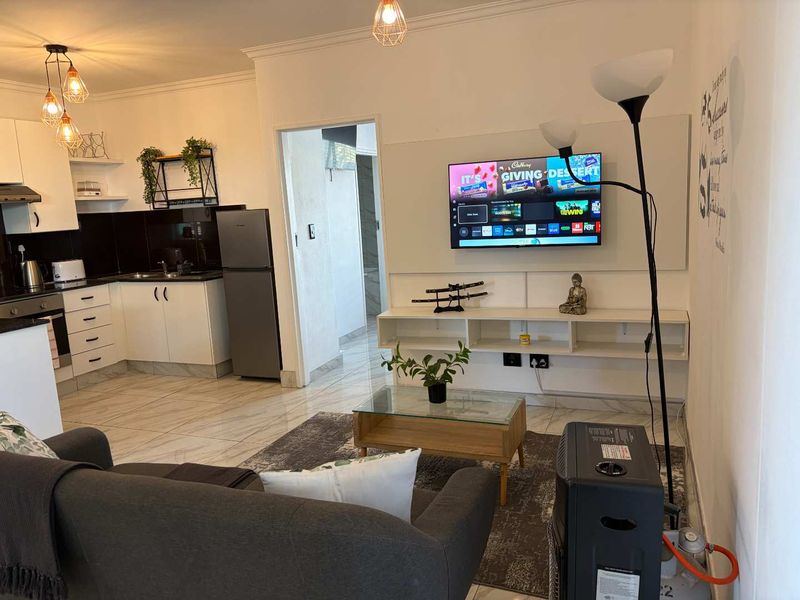 An open-plan living and kitchen area featuring modern white cabinetry, tiled flooring, and a wall-mounted media console in a well-maintained apartment setting.