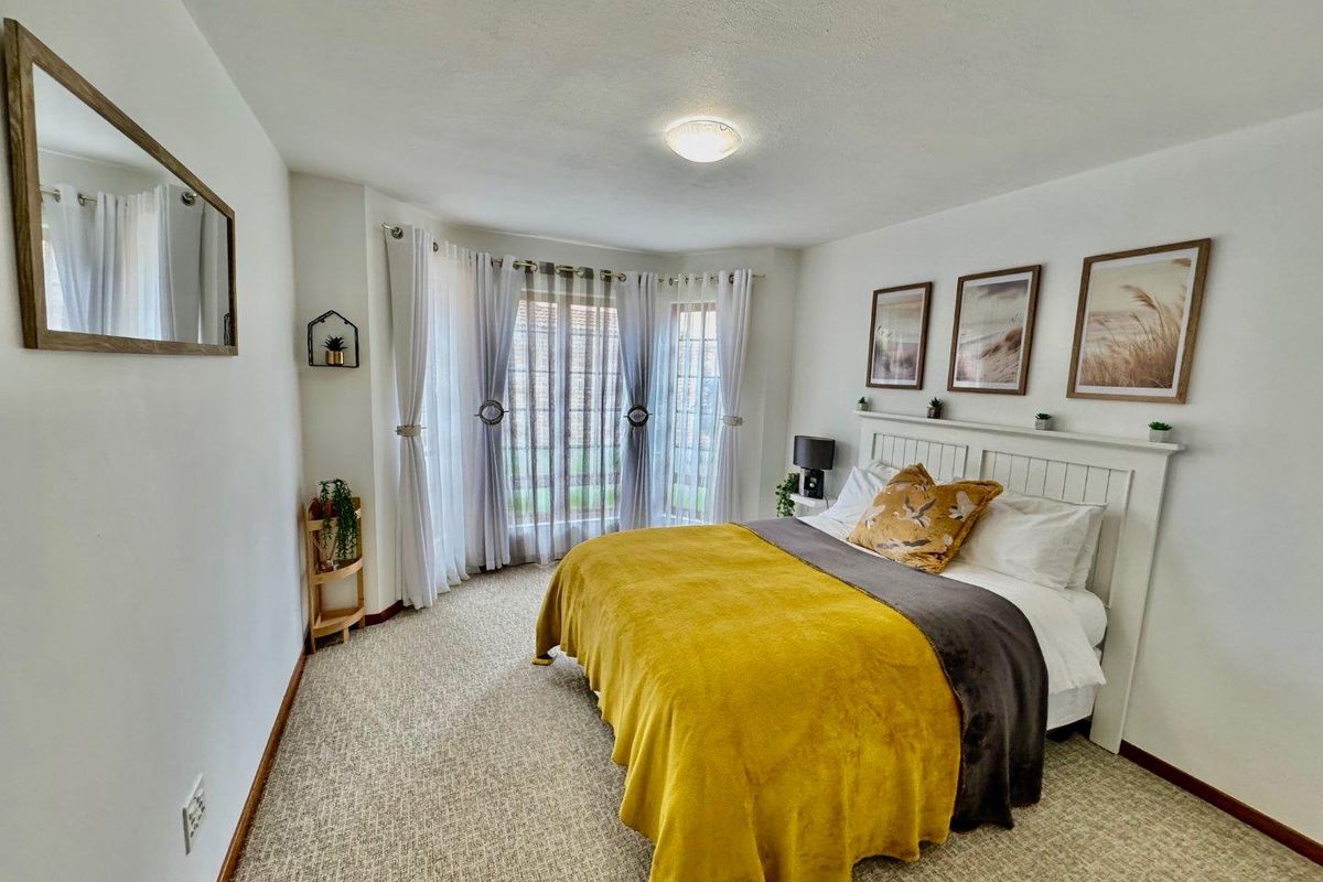 A well-maintained bedroom featuring a large bay window, neutral carpeting, and a built-in headboard, offering a bright and comfortable living space.
