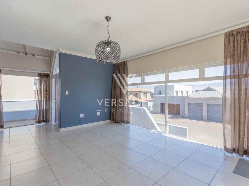 Spacious, light-filled living area featuring neutral tiled flooring, a modern accent wall, and large glass doors leading to an outdoor patio.